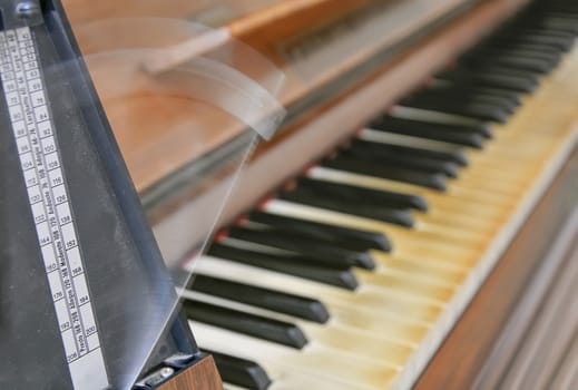 Antique metronome marks the rhythm of the music on an old wooden piano