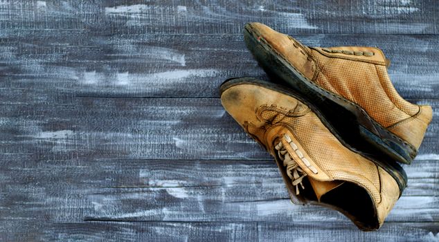 On a wooden background a pair of brown shoes. One pair of leather sneakers is very worn. Black Friday - time to buy new sneakers. Sneakers in the upper right corner are laced with laces. Close-up. Copy space.