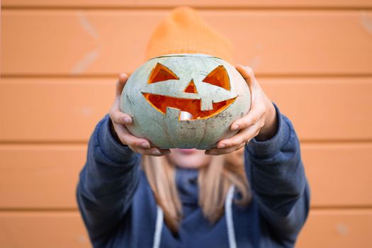 Woman in casual clothes and hat holding Halloween pumpkin over orange wall background with copy space for text