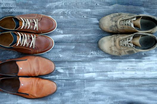 On a wooden background are three pairs of brown shoes. One pair of leather sneakers is very worn, the second is in good condition, the third pair of shoes is new. Black Friday - time to buy new sneakers. Close-up. Copy space