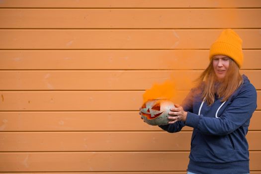 Grumpy woman with halloween pumpkin with orange smoke, funny shot of failure