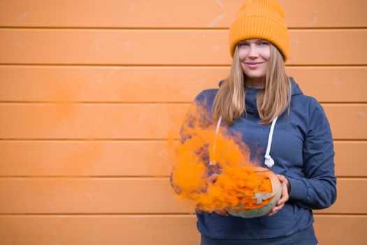 Woman in casual clothes and hat holding Halloween pumpkin over orange wall background with copy space for text