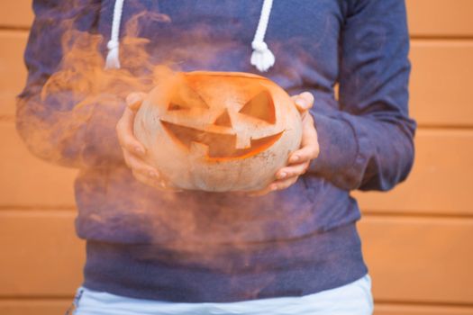 Woman in casual clothes and hat holding Halloween pumpkin over orange wall background with copy space for text