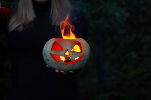 Woman with burning pumpkin in hand dark halloween background with copy space for text
