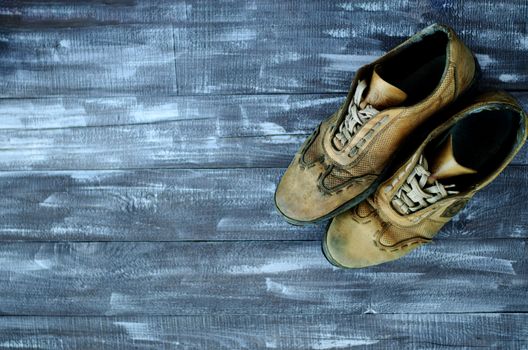 On a wooden background a pair of brown shoes. One pair of leather sneakers is very worn. Black Friday - time to buy new sneakers. Sneakers in the upper right corner are laced with laces. Close-up. Copy space.