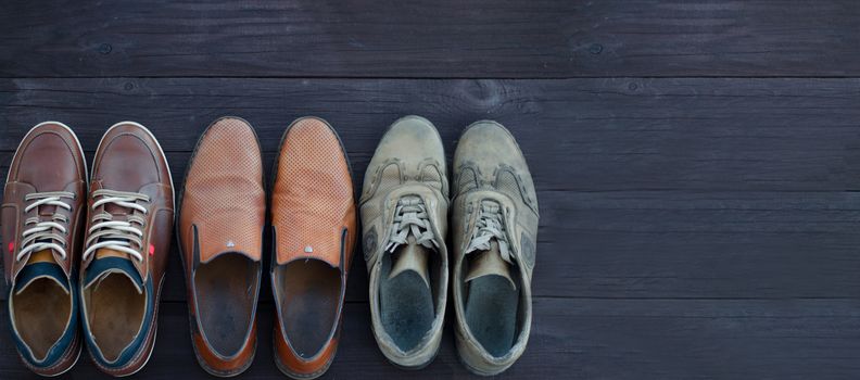 On a wooden background are three pairs of brown shoes. One pair of leather sneakers is very worn, the second is in good condition, the third pair of shoes is new. Black Friday - time to buy new sneakers. Close-up. Copy space