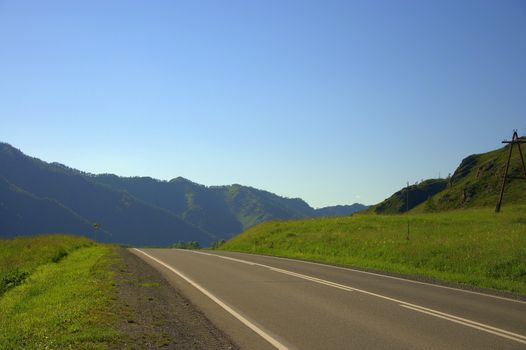 A direct asphalt road goes through the flight valley towards the mountain ranges. Altai, Siberia, Russia.