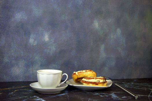 A cup of black coffee and a saucer with two fresh cinnamon rolls. Close-up.