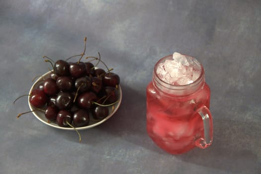A full saucer of ripe cherries and a glass mug with cherry juice with ice. Close-up.