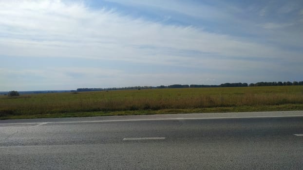 Fragment of an asphalt road passing near the field. Autumn landscape.