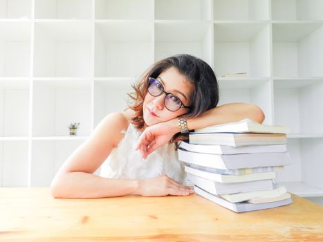 Beautiful women in glasses crushed on the table by a lot of books, very stressed of the study.
