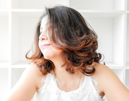 Close up portrait of a beautiful woman smiling, with white bookshelf background.
