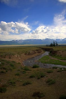 View of the stream flowing through the steppe with mountains covered in snow.