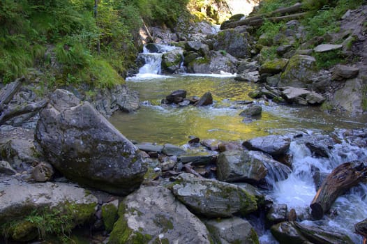 A small waterfall on a small mountain river flowing through stony banks.