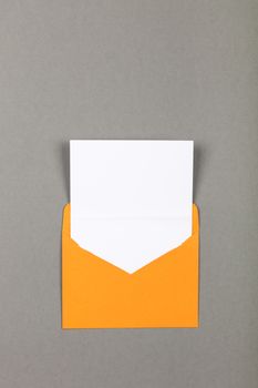 One open blank vivid yellow envelope with white paper over grey background, flat lay, directly above