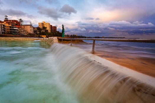 High tide brings the overflow waterfalls that flush the ocean rock pool at Manly.  Stormy rain clouds hover out to sea.