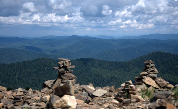 Two cairns on the edge of a mountain peak with beautiful views of the valley under the clouds. Altai, Siberia, Russia.