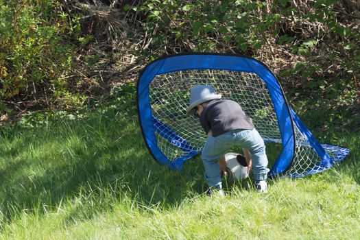 Little boy with hat and sunglasses while playing football in a garden