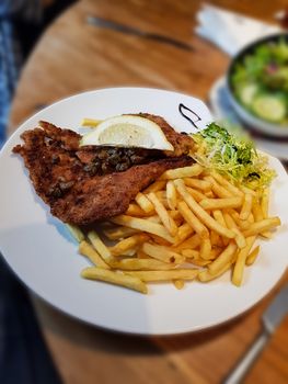 Wienerschnitzel, served with French fries and salad. Natural wood background. front view