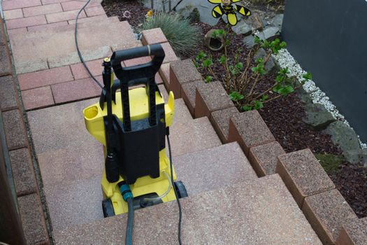 Yellow pressure washer on a staircase with hose and pistol