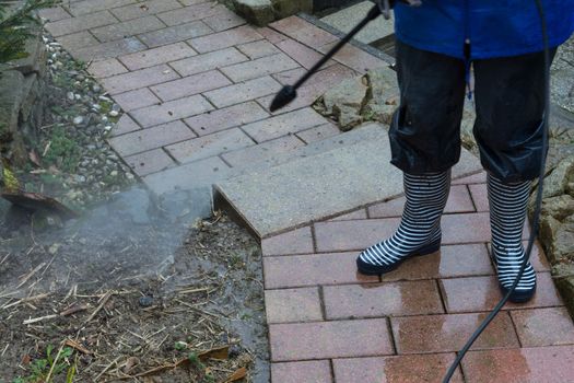 Woman cleans stone slabs with a pressure washer