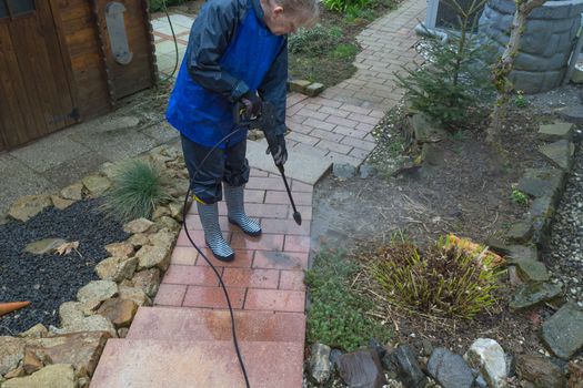 Woman cleans stone slabs with a pressure washer