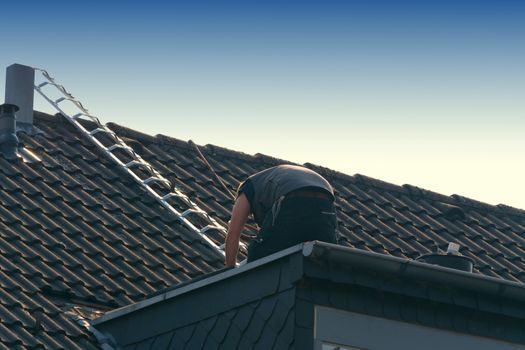 Roofer works on an unfinished roof. Installs roof shingles