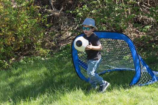 Little boy with hat and sunglasses while playing football in a garden