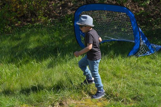 Little boy with hat and sunglasses while playing football in a garden