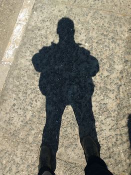 Shadow in silhouette of man standing in sunny day on rustic floor.
