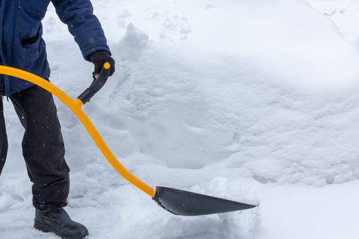 A man cleans snow in the yard with a shovel after a heavy snowfall.