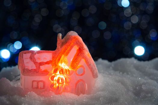 Glowing toy house in the snow on the background of Christmas lights. Festive, Christmas or New Year concept.
