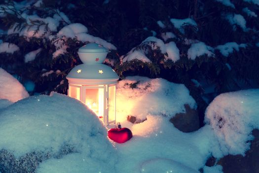 Lantern with a burning candle under a snow-covered Christmas tree in the courtyard of the house in the snowdrifts.