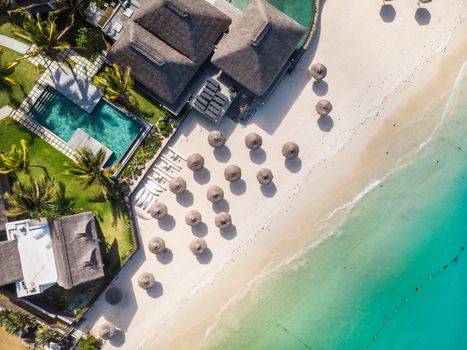 Aerial view of beautiful tropical beach front hotel resort with swimming pool, palm leaves umbrellas and turquoise sea. Paradise destination for vacations in Mauritius.