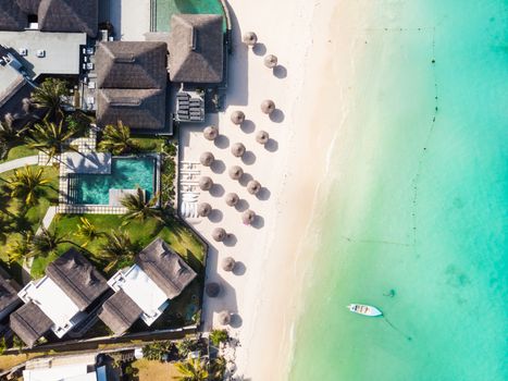 Aerial view of beautiful tropical beach front hotel resort with swimming pool, palm leaves umbrellas and turquoise sea. Paradise destination for vacations in Mauritius.