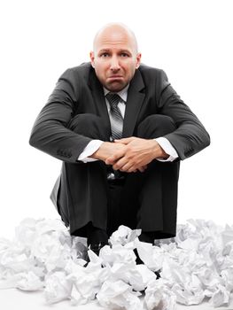 Business problems and failure at work concept - unhappy tired or stressed businessman in depression sitting down floor on crumpled torn paper document heap white isolated