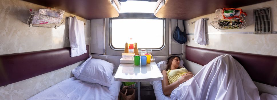 Panorama of the interior of a reserved seat train car, a girl sleeping on one of the lower shelves