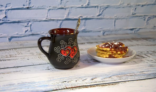 A mug of herbal tea with lemon and saucer with a stack of waffles with strawberry jam. Close-up.