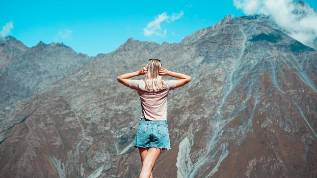 Woman hiking in mountains at sunny day time. View of Kazbegi, Georgia. Beautiful natural mountain background