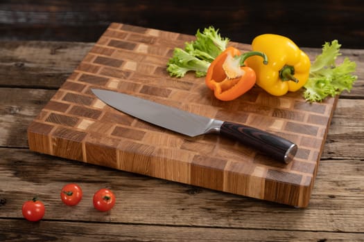 Red, ripe, bright tomatoes and peppers lie on a wooden cutting board near the kitchen knife. Cutting vegetables for cooking. Fresh, ripe, tasty, natural vegetable.