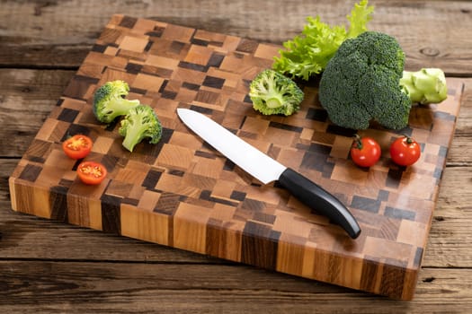 Bright ripe, broccoli, tomatoes and peppers lie on a wooden cutting board near the kitchen knife. Cutting vegetables for cooking. Fresh, ripe, tasty, natural vegetable.