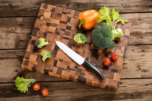 Bright ripe, broccoli, tomatoes and peppers lie on a wooden cutting board near the kitchen knife. Cutting vegetables for cooking. Fresh, ripe, tasty, natural vegetable.