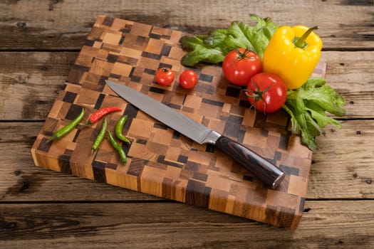 Red, ripe, bright tomatoes and peppers lie on a wooden cutting board near the kitchen knife. Cutting vegetables for cooking. Fresh, ripe, tasty, natural vegetable.