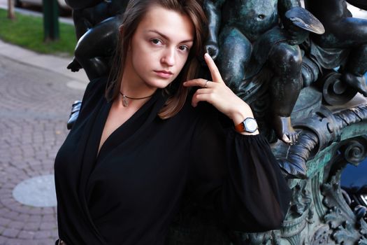 Beautiful young woman near old iron sculpture with angels