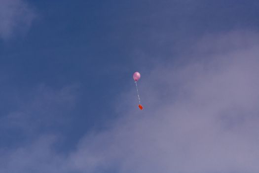 Pink balloon with ribbon and greeting card in front of blue sky