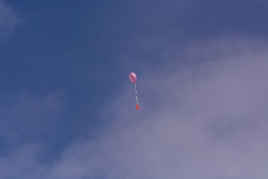 Pink balloon with ribbon and greeting card in front of blue sky