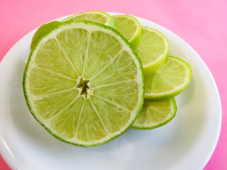 Sliced lime slices on white plate with pink background.