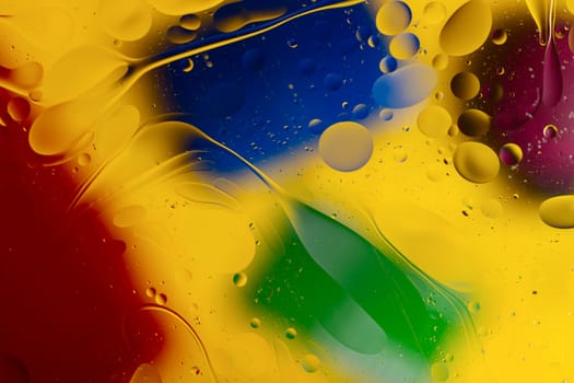 Abstract oil spots in motion on water on blurred yellow background. Red, green, purplee and blue spots on blurred background. Photo with small depth of field.