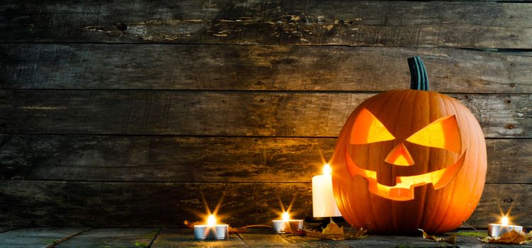 Halloween pumpkin head jack lantern and candles on wooden background