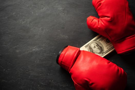 Boxing Gloves holds the dollar banknote on black cement background. Concept of boxing betting or business struggle. Top view and copy space for text.